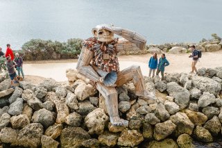 Tourists looking at wooden giant construction, sitting on rocky outcrop