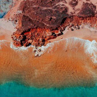 Birds eye view of colourful coastline - red rocks, orange sand and blue-green water
