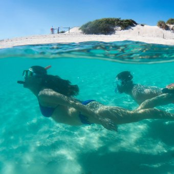 Two people snorkelling in the ocean next to a sandy island