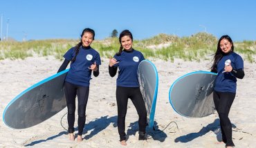 Three happy students with surfboards at beach
