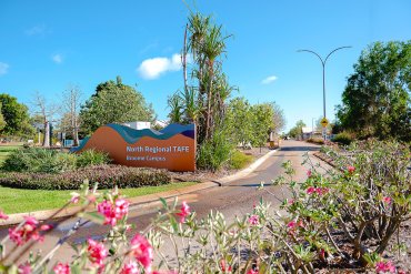 Colourful flowers in foreground, Broome TAFE campus sign and entry road in background
