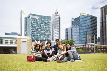 Group of six students sitting together in outdoor space near central Perth. Tall buildings in background.