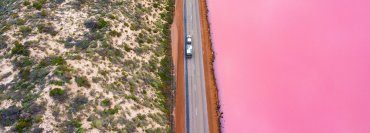 Aerial view of car on road between pink lake and grassy hill