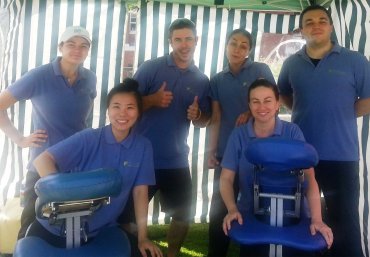 A group of 5 individuals are in the photo. On the front left is South Metropolitan TAFE lecturer Jinjoo Park. Everyone in the photo are wearing blue polo shirts. At the front of the image are two massage beds. Everyone is smiling. 