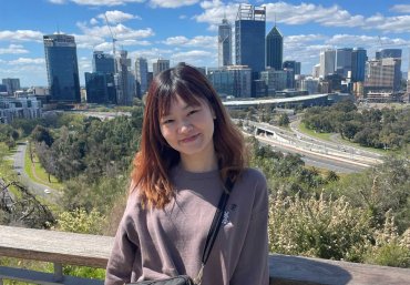 Student Sachiho looks towards the camera smiling. In the background there's an impressive view of the Perth city skyline.